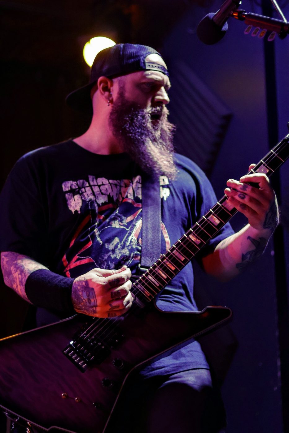 Nate Laff playing an Explorer-style guitar on stage under purple light